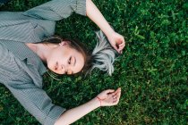 Top view of trendy businesswoman resting, raising hands and lying on green grass — Stock Photo