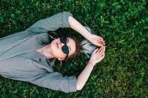 Top view of trendy businesswoman resting, raising hands and lying on green grass — Stock Photo