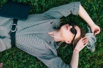 Vista superior da mulher de negócios na moda descansando, levantando as mãos e deitado na grama verde com laptop — Fotografia de Stock