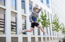 Trendige Geschäftsfrau hält Tablet und Sonnenbrille in der Hand, springt auf Geschäftsbereich und schaut weg — Stockfoto