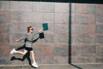 Vista lateral da mulher de negócios elegante pulando ao longo da parede de mármore e acenando as mãos com tablet — Fotografia de Stock