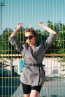 Mulher de negócios na moda olhando para a câmera em óculos de sol e inclinando-se na treliça amarela em dia brilhante no playground — Fotografia de Stock