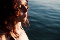 Vue latérale de belle dame aux yeux fermés debout dans de l'eau de mer propre par une journée ensoleillée — Photo de stock