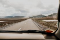 Carretera asfaltada que atraviesa llanuras y colinas frente al vehículo en un día gris cubierto en Marruecos. - foto de stock