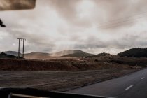 Carretera asfaltada que atraviesa llanuras y colinas frente al vehículo en un día gris cubierto en Marruecos. - foto de stock
