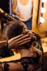Back view of brunette woman fixing hair while crop stylist standing behind and reflecting in mirror in dressing room — Stock Photo
