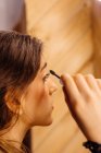 Side view of crop brunette attractive woman looking in mirror doing makeup applying mascara on eyelashes — Stock Photo