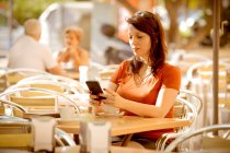 Erwachsene ruhige Frau in Freizeitkleidung surft im Internet, während sie auf der gemütlichen Café-Sommerterrasse sitzt und auf Bestellung wartet — Stockfoto