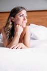 Ragazza bionda sorridente su un letto con lenzuola bianche illuminate dalla luce della finestra al mattino — Foto stock