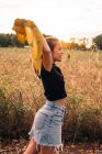 Vista lateral do conteúdo mulher bronzeada em desgaste casual decolando camisa perto de cerca de arame metálico no campo rural — Fotografia de Stock
