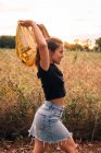 Side view of content bronzed woman in casual wear taking off shirt near metal chain link fence on rural field — Stock Photo