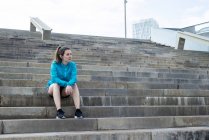 Спортивная женщина, сидящая на лестнице, отводя взгляд — стоковое фото