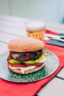 Delizioso cheeseburger fatto in casa con lattuga, pomodoro e salsa su piatto verde servito con bicchiere di birra . — Foto stock