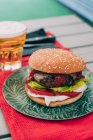 Köstliche hausgemachte Rindfleisch-Burger mit Salat, Tomaten und Sauce auf grünem Teller serviert mit einem Glas Bier. — Stockfoto