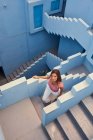 De cima vista da jovem mulher andando no andar de cima no edifício azul moderno e olhando para a câmera — Fotografia de Stock