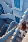 Зверху ми бачимо молоду жінку, яка йде нагору на сучасному синьому будинку і дивиться кудись убік. — стокове фото