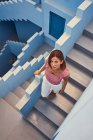 De cima vista da jovem mulher andando no andar de cima no edifício azul moderno e olhando para a câmera — Fotografia de Stock