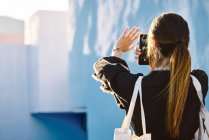 Vue arrière de la femme debout sur un bâtiment bleu et prenant des photos avec un téléphone mobile — Photo de stock