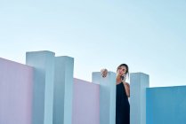 Mulher de pé no topo do edifício azul e falando por smartphone — Fotografia de Stock