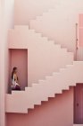 Seitenansicht einer Frau, die auf einem modernen rosa Gebäude die Treppe hinuntergeht, während sie in die Kamera schaut — Stockfoto