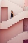 Вид збоку жінки, що йде вниз на сучасну рожеву будівлю — стокове фото