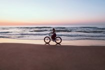 Joyful woman riding bicycle along peaceful beach — Stock Photo