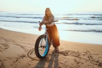 Joyful woman riding bicycle along peaceful beach — Stock Photo