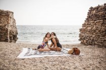 Vista lateral de las mujeres jóvenes con estilo en trajes de baño relajante en la orilla del mar, tomando una foto por teléfono inteligente - foto de stock