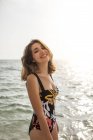 Приваблива щаслива жінка в стильному купальнику стоїть і дивиться на камеру в сонячний день — стокове фото