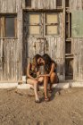 Zärtliches weibliches Paar, das an einem alten Holzschuppen sitzt, Händchen hält und mit der Stirn berührt — Stockfoto