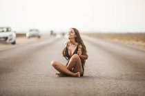 Attractive young woman smiling and sitting on road with white stripes — Stock Photo