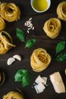 Rolos de massa crus tagliatelle com folhas de manjericão, alho e queijo na mesa — Fotografia de Stock