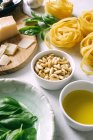 Pine nuts in bowl and ingredients for pesto sauce with tagliatelle on table — Stock Photo