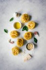 Nester von Tagliatelle-Pasta mit Basilikumblättern und Knoblauch auf dem Tisch — Stockfoto