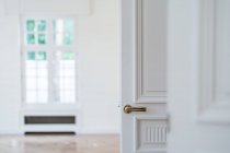 Porta branca aberta com alça dourada em interior minimalista claro no fundo embaçado — Fotografia de Stock