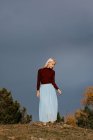 Elegant young woman in blue long skirt and turtleneck walking along rural area on chilly day — Stock Photo