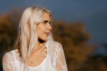 Ніжна жінка з білим світлим волоссям, що розмірковує, стоячи в сільській місцевості з апельсиновим листям — стокове фото