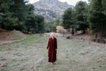 Босоніжка блондинка в червоному пальто, що йде вздовж сосен в холодний день — стокове фото