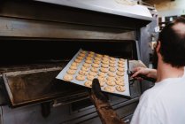 Erntehelfer guckt in professionellen Backofen, während er in Bäckerei arbeitet — Stockfoto