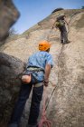 Aventureiros escalando montanha vestindo arnês de segurança contra paisagem pitoresca — Fotografia de Stock
