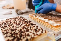 Anonymous cook squeezing fresh pastry dough on tray with paper while working on blurred background of bakery — Stock Photo