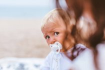 Blond baby with pacifier on the beach — Stock Photo