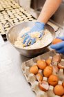 Pastelero de cosecha en guantes y mezcla uniforme y amasar masa fresca suave mientras se prepara la pastelería en la panadería - foto de stock