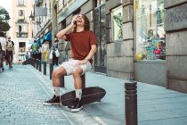 Alegre hombre casual riendo y hablando en el teléfono inteligente mientras está sentado en baluster en la calle de la ciudad - foto de stock