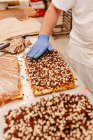 Неузнаваемый кондитер в перчатках, украшающий вкусный свежий торт шоколадной крошкой во время работы на пекарне — стоковое фото