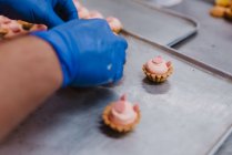 De arriba pastelero irreconocible decorando pastelería rosa en bandeja mientras se trabaja en panadería - foto de stock
