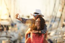 Woman carrying girlfriend on back and taking selfie — Stock Photo