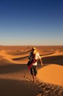 Невпізнаваний турист з простягнутими обіймами стоїть на тлі яскравого безхмарного сонячного неба в пустелі — стокове фото
