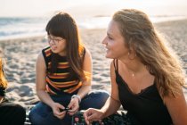 Una hermosa chica rubia charlando con su grupo de amigos en la playa, junto a su amiga asiática - foto de stock