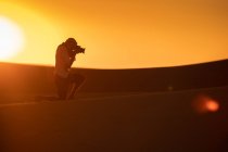 Unrecognizable traveler silhouette taking pictures of dunes while standing on sand in amazing desert — Stock Photo
